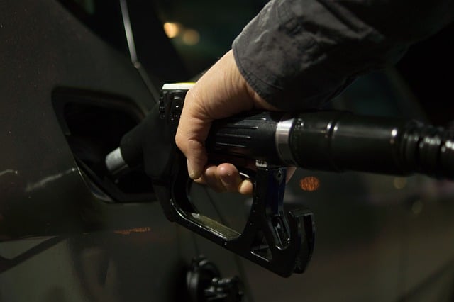 A imagem mostra o bico de posto de gasolina abastecendo um carro com destaque, simbolizando a notícia sobre a redução histórica de 13 centavos por litro no preço da gasolina.