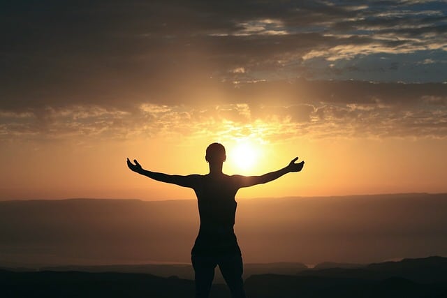 Foto de homem de braços abertos apreciando o pôr do sol expressando sua gratião